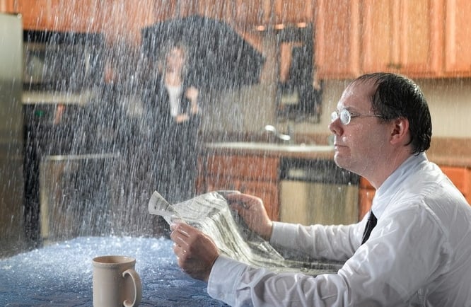 Man overwhelmed by indoor water damage due to a roof leak, highlights the importance of insurance claim assessment