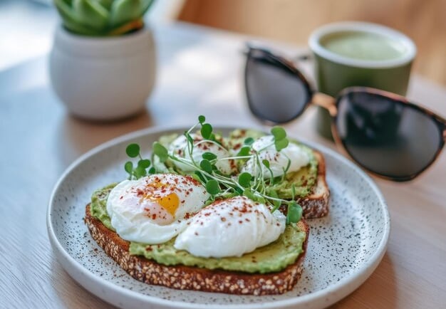 Two slices of whole-grain toast topped with creamy mashed avocado, fresh radish microgreens, and a d