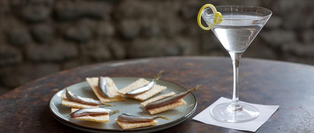 anchovies on water crackers plated on a rustic table next to a Dry Martini with a lemon twist