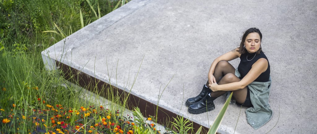 A stylish woman sitting on a concrete rooftop garden with vibrant wildflowers and green plants.