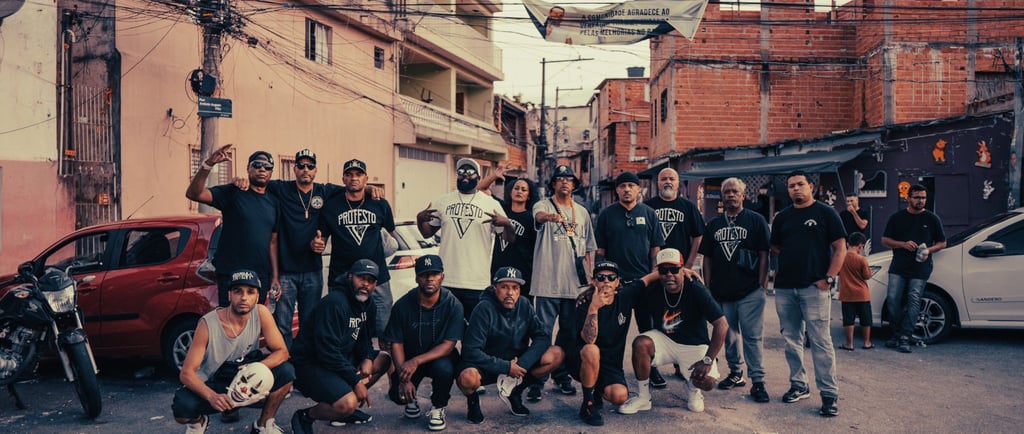 A group of Brazilian hip-hop artists posing in a neighborhood street with urban buildings.
