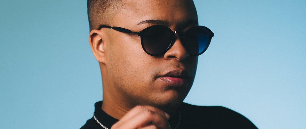 Young man with a faded haircut wearing black sunglasses and a gold chain on a blue background.