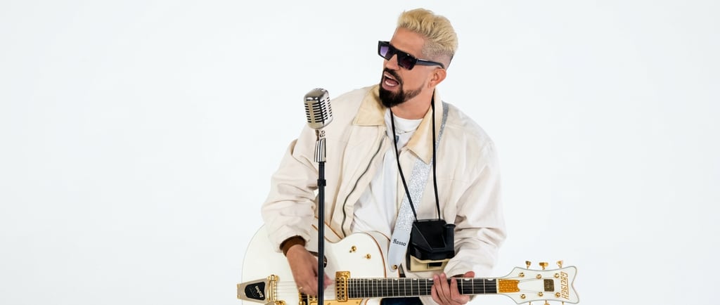 Musician with blonde hair playing a white Gretsch electric guitar and singing into a vintage microphone.