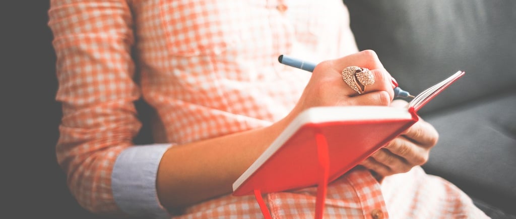 a woman in a plaid shirt and glasses is writing a diary or notebook