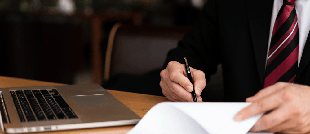 Advogado escrevendo em um papel em uma mesa com notebook