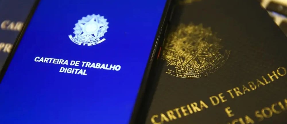 Celular com a carteira de trabalho digital aberta e a versão impressa ao lado