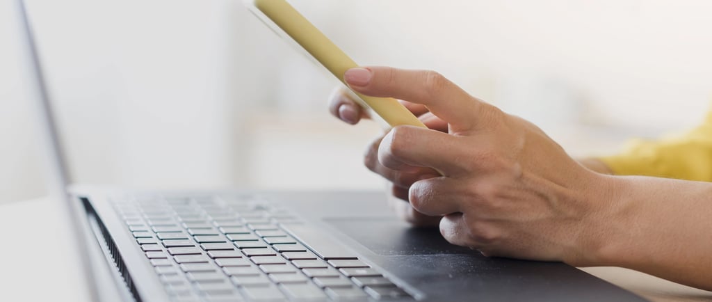 Notebook na mesa e mulher com celular na mão