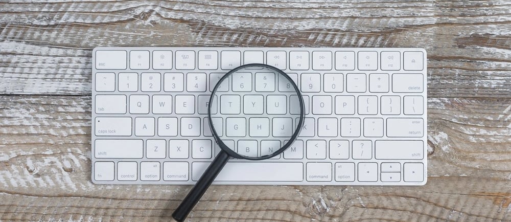 Teclado de computador e lupa em cima de mesa de madeira