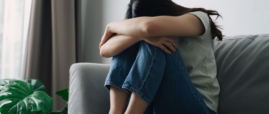 Frau sitzt auf einem Sofa, hat die Knie angezogen und den Kopf auf die Arme gelegt – Ausdruck von Er