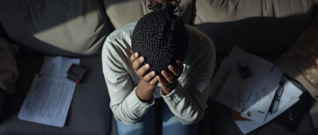 Stressed woman sitting on a couch holding her head near scattered paperwork and documents.