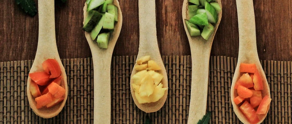 Flat lay of fresh chopped vegetables on wooden spoons with green neem leaves on a rustic mat.