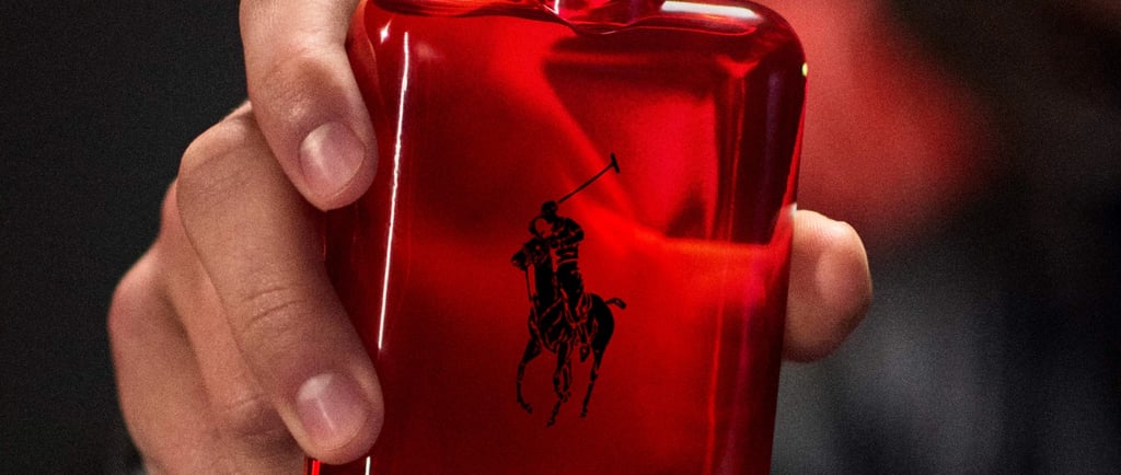 A man's hand holding a red Ralph Lauren Polo Red perfume bottle with the iconic polo player logo.