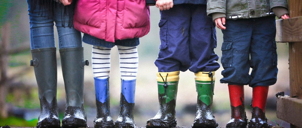 Four children standing in a row wearing colorful winter coats and muddy rain boots outdoors.