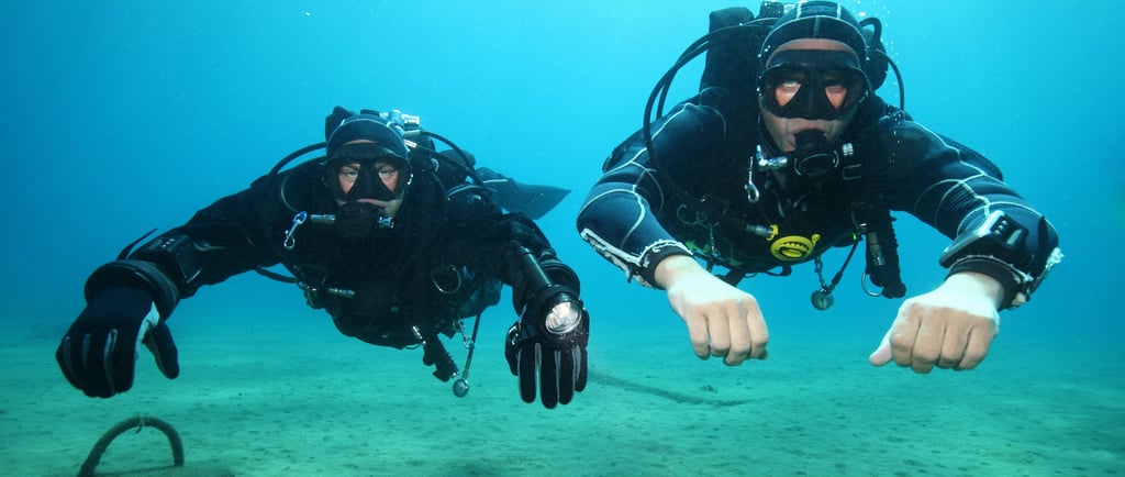 two scuba divers in full bodysuits and diving gear