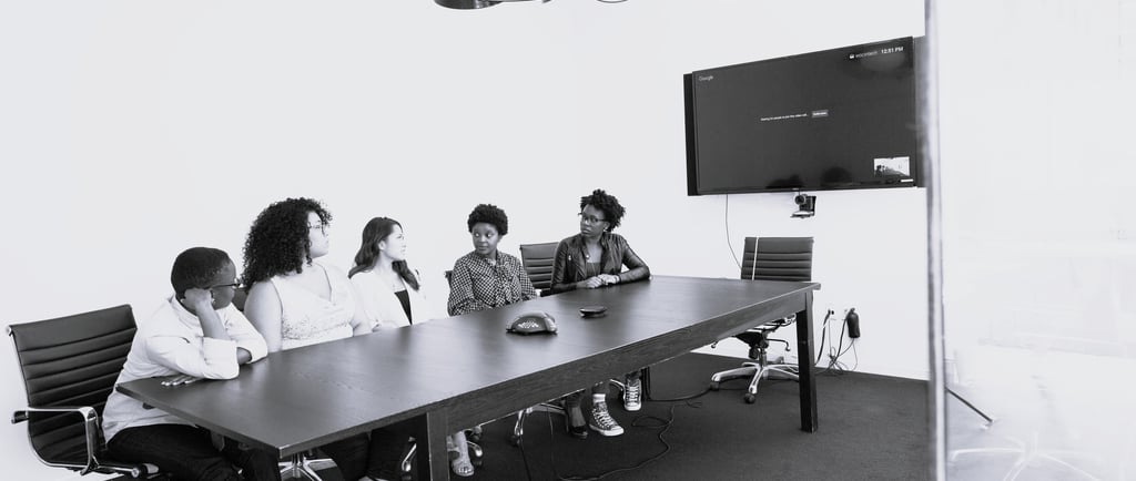 Professional meeting scene where one employee hesitates to speak while others face forward