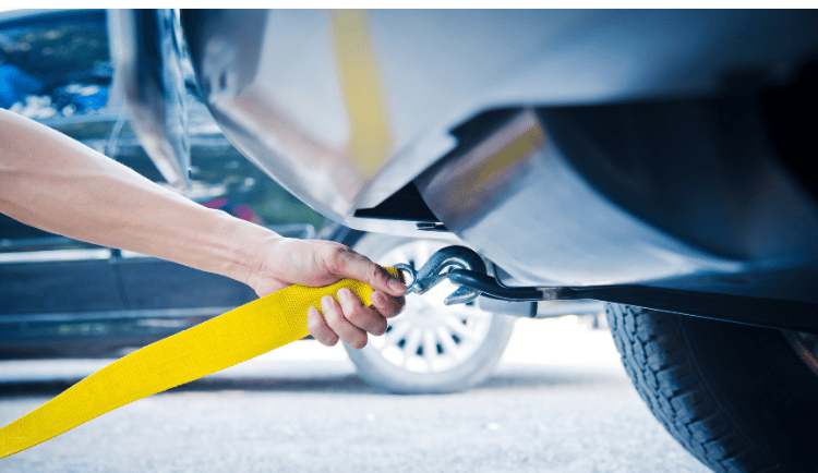 Image of a tow truck operator hooking a winch to the under carriage of a stranded vehicle.