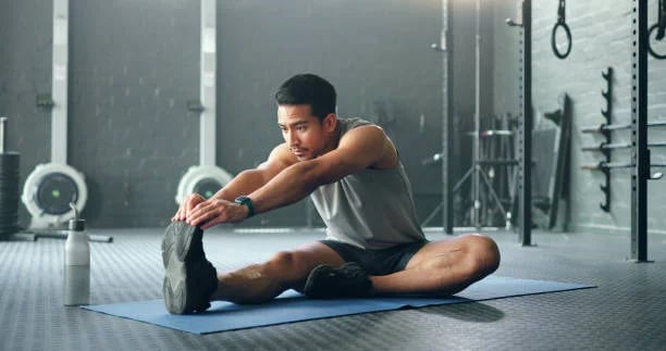 a man is stretching his legs on a mat with a bottle of water