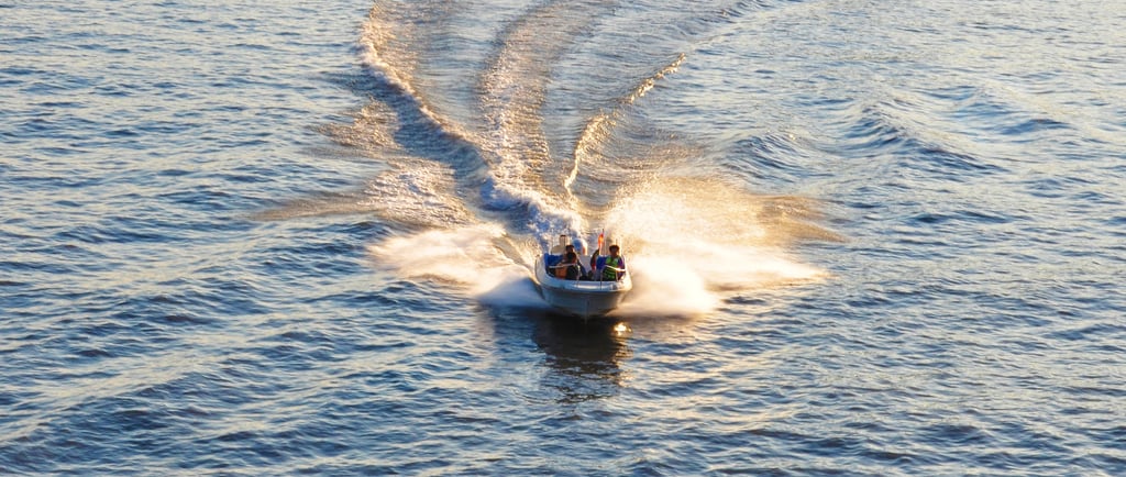 A motorboat speeds across blue water at sunset, leaving a white wake in its trail.