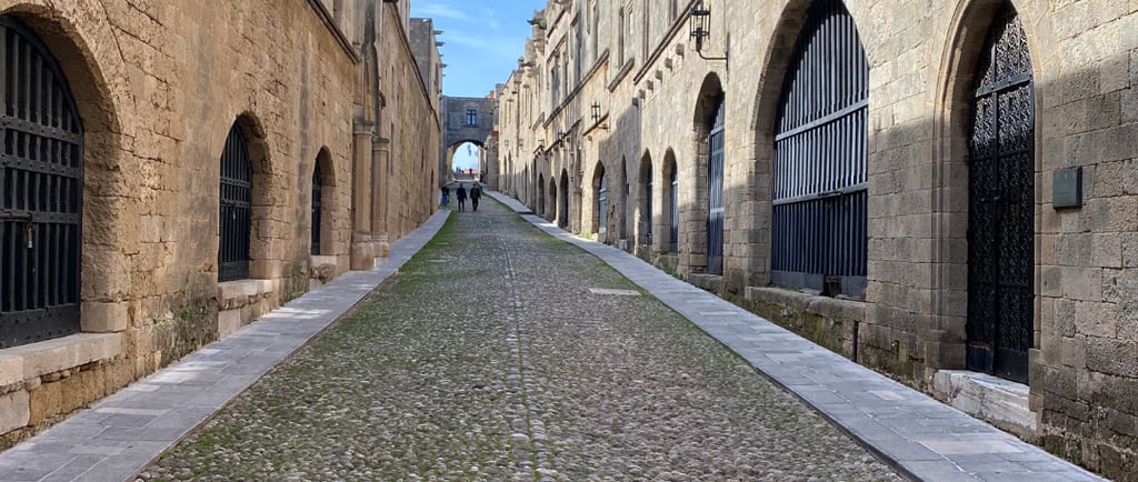 Historic cobblestone street of the Knights in Rhodes Old Town with medieval stone architecture and arched windows.