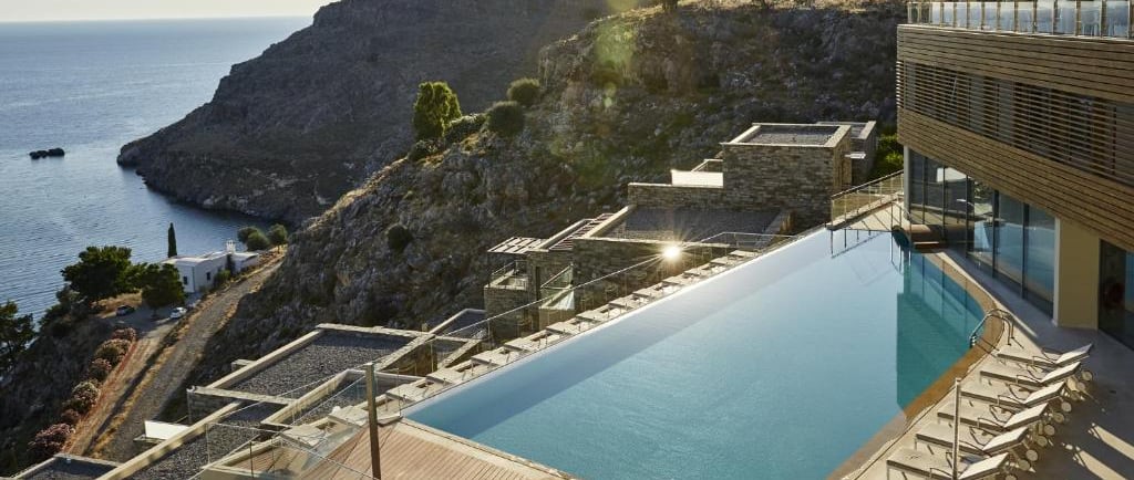 Luxury infinity pool at a cliffside Mediterranean resort overlooking the blue sea and rugged mountains.