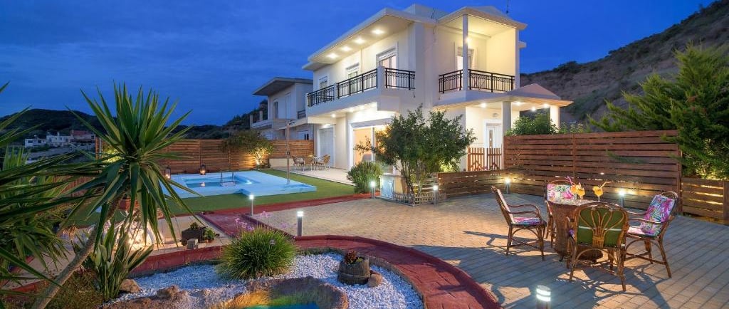 Luxury modern villa with outdoor pool, garden pond, and patio seating at sunset.