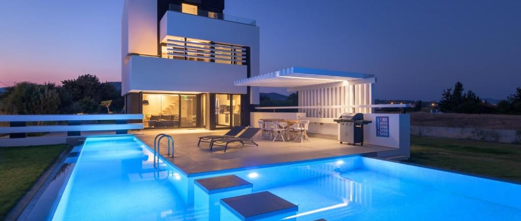 Luxury modern villa with an illuminated infinity swimming pool and outdoor patio at twilight.