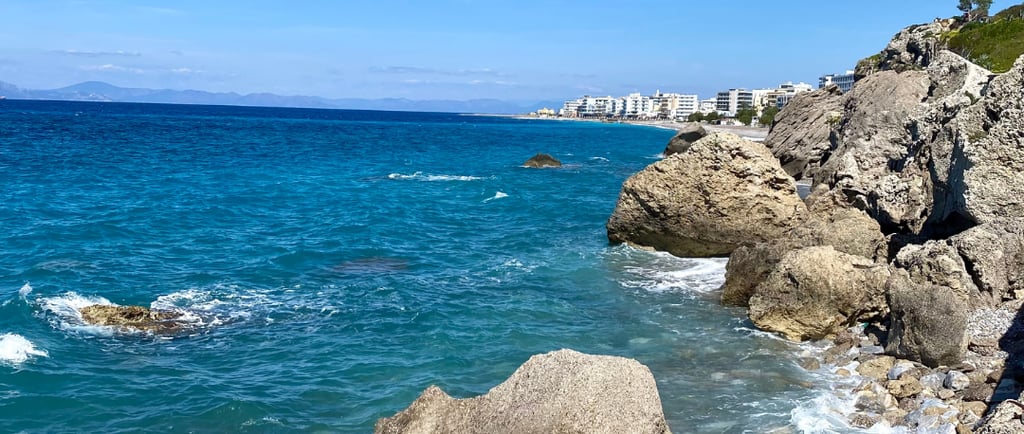 blue sea, some rocks and rhodes city on background
