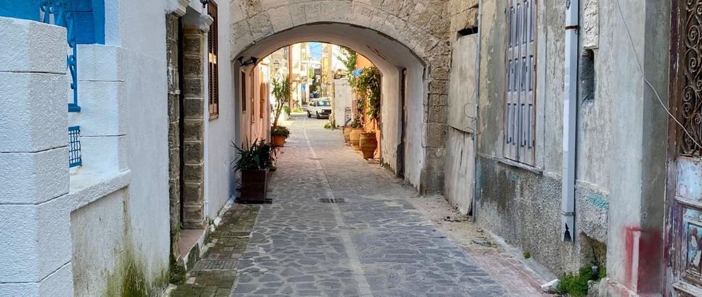 A narrow cobblestone street in Rhodes Old Town featuring a stone archway and Mediterranean architecture.