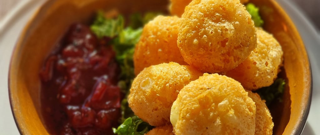 Golden fried cheese balls appetizer served with cranberry sauce and fresh greens in a ceramic bowl.