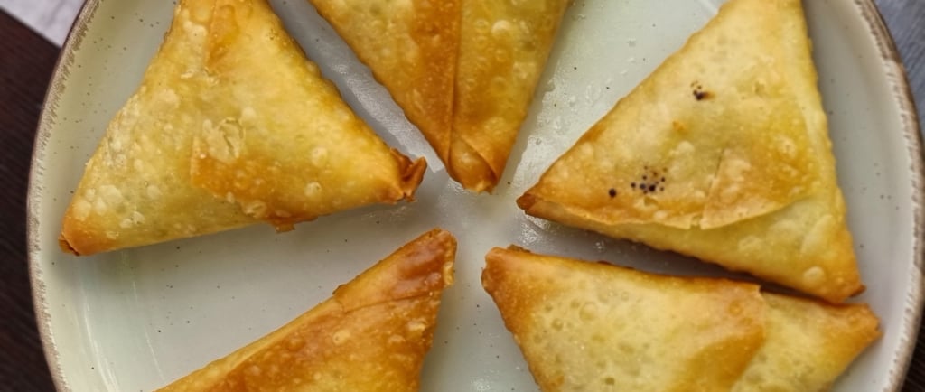 Five golden-brown fried vegetable samosas served on a white ceramic plate.