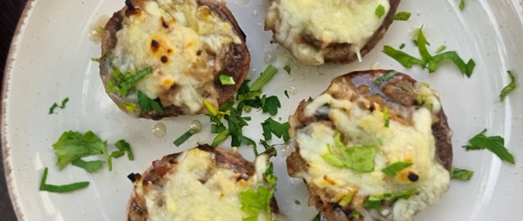 Four baked mushrooms stuffed with melted cheese and fresh herbs on a white ceramic plate.