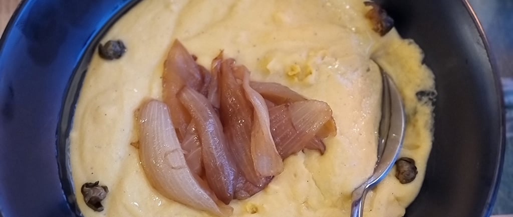 Greek fava dip in a black bowl topped with caramelized onions and capers.