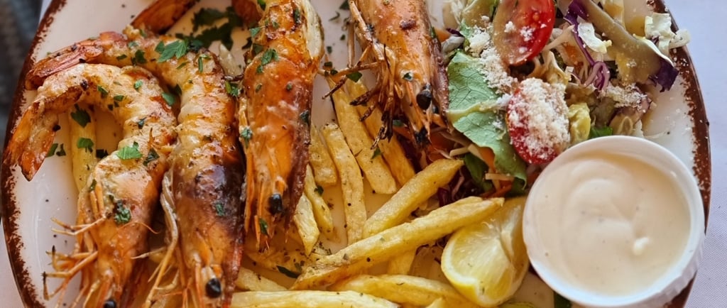Grilled prawns served with crispy french fries, fresh garden salad, and creamy dipping sauce on a white plate.