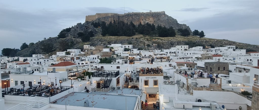Panoramic view of white houses in Lindos village with the ancient Acropolis on a hill in Rhodes, Greece.