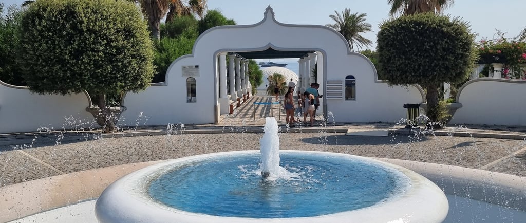 A tiered water fountain at Kallithea Springs in Rhodes featuring white arches and palm trees.