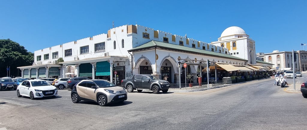 White architecture and traditional market building with a dome in a sunny Rhodes city square with cars.