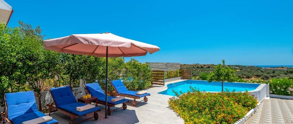 Luxury villa terrace with blue lounge chairs, pink umbrella, and a private swimming pool.