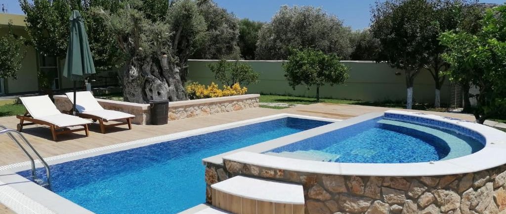 Luxury backyard swimming pool with a stone-clad hot tub, sun loungers, and lush garden landscaping.