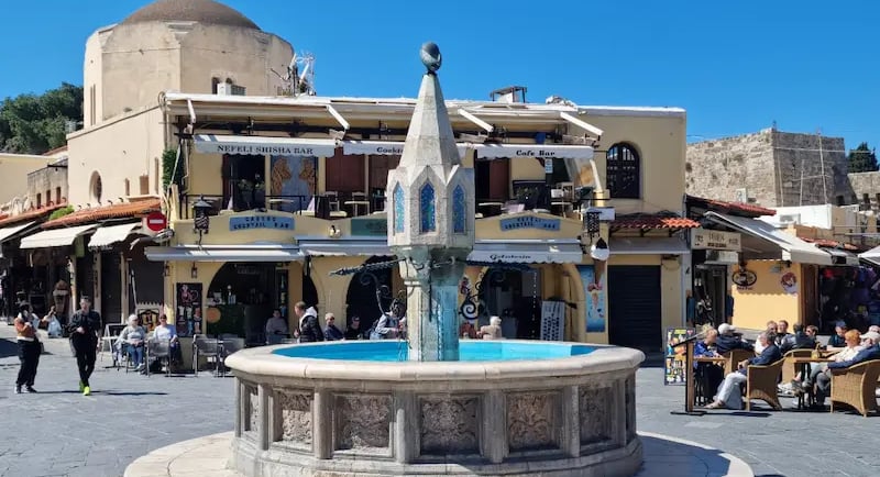 Historic Castellania Fountain in Hippocrates Square under a blue sky in Rhodes Old Town, Greece.