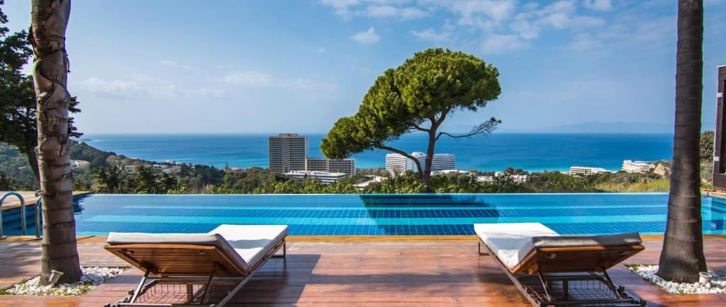 Luxury infinity pool with sun loungers overlooking the ocean at a Mediterranean resort.