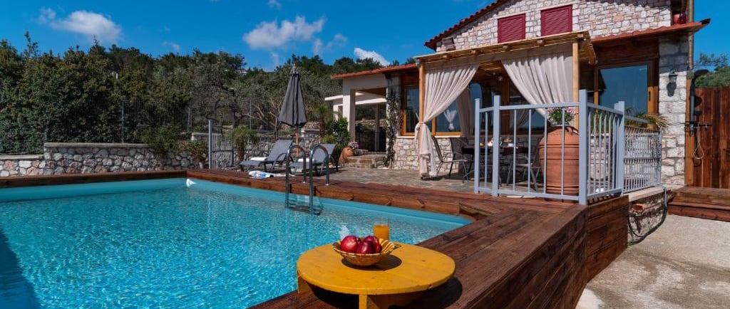 Luxury stone villa with a private swimming pool, wooden deck, and outdoor patio under a blue sky.