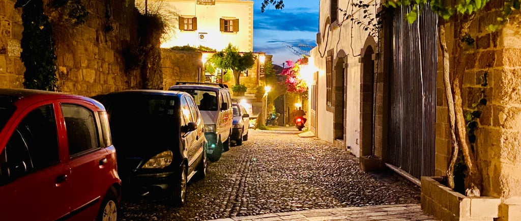 Cars parked along a cobblestone street in a historic European town at twilight.