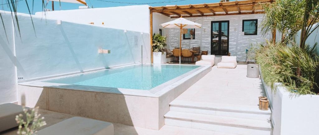 Luxury villa patio with a private swimming pool, white lounge chairs, and an outdoor terrace under a clear blue sky.