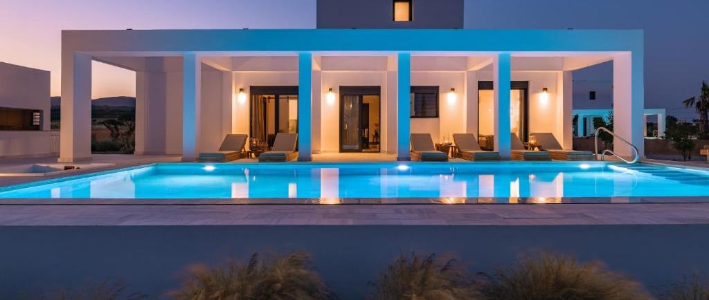 Luxury modern villa with a glowing swimming pool and sun loungers at twilight.