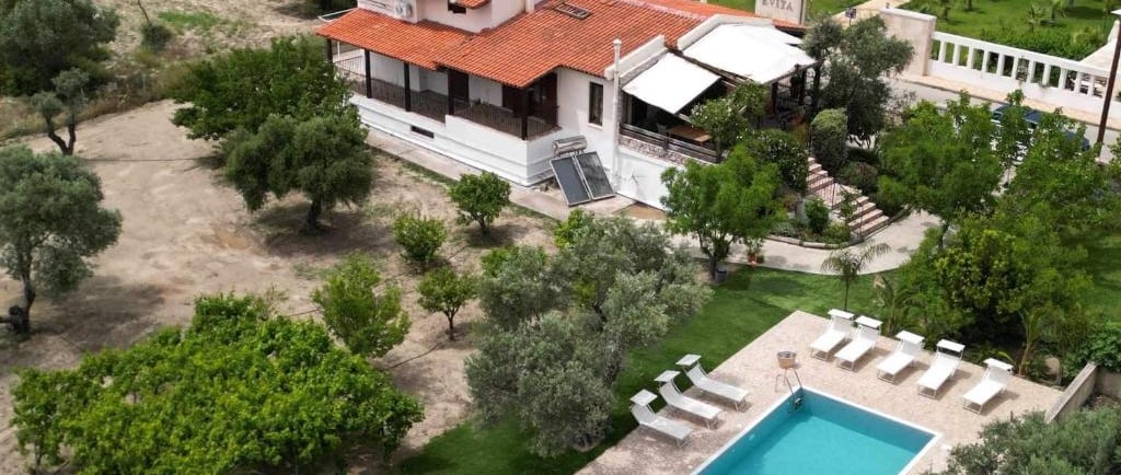 Aerial view of a Mediterranean villa with a swimming pool, sun loungers, and lush green olive trees.