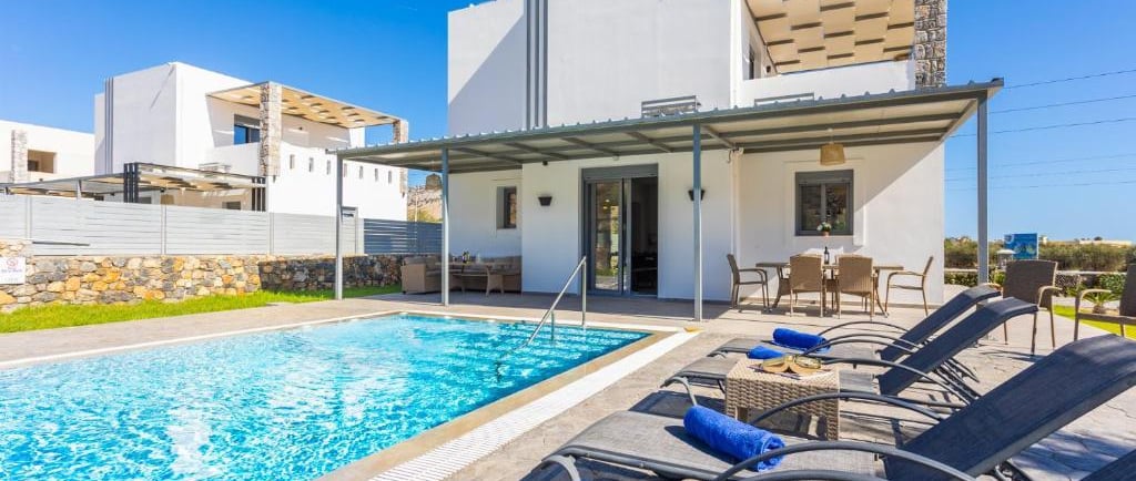 Luxury modern villa with private swimming pool, sun loungers, and outdoor dining patio under a clear blue sky.