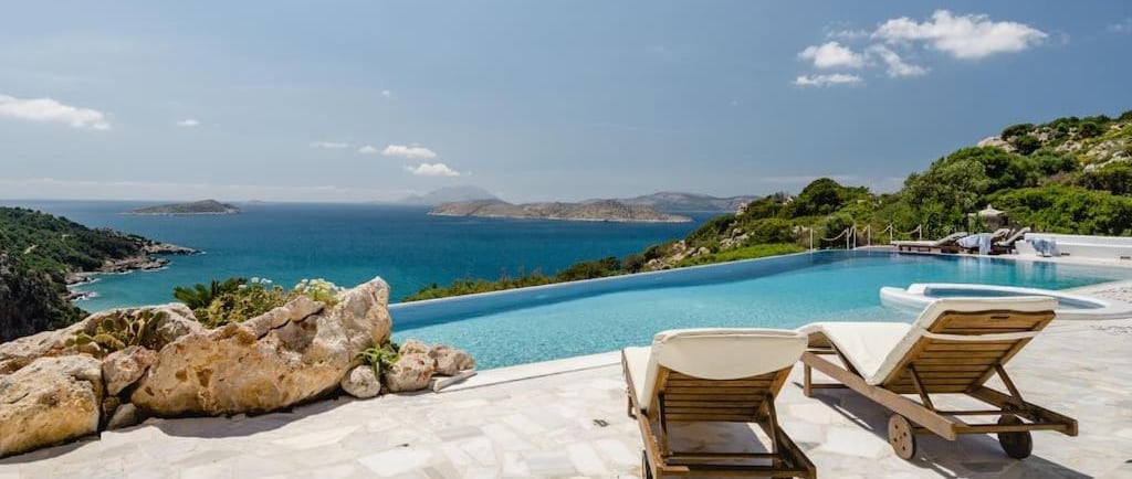 Luxury infinity pool and sun loungers overlooking the Mediterranean Sea and Greek islands.