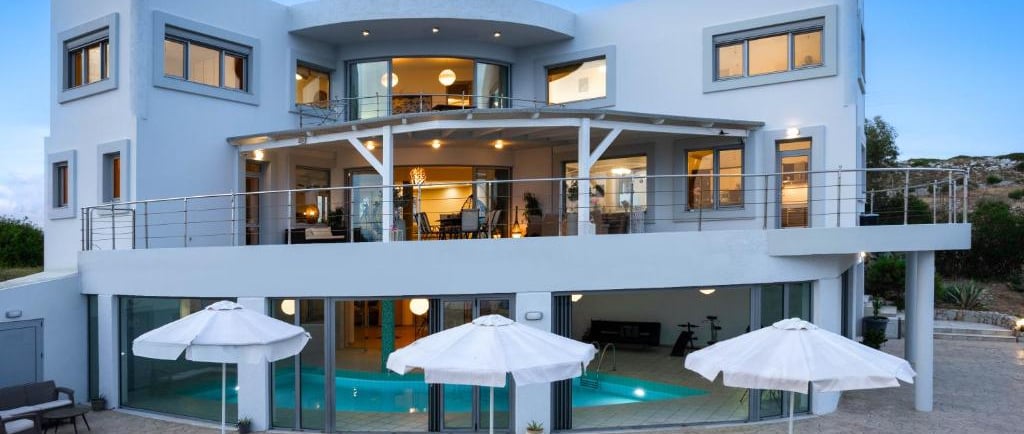 Luxury modern villa with a private swimming pool, sun loungers, and patio umbrellas at dusk.