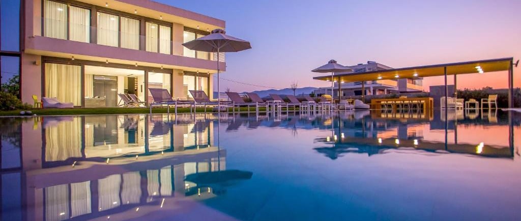 Luxury modern villa with a large infinity swimming pool and lounge chairs at sunset.