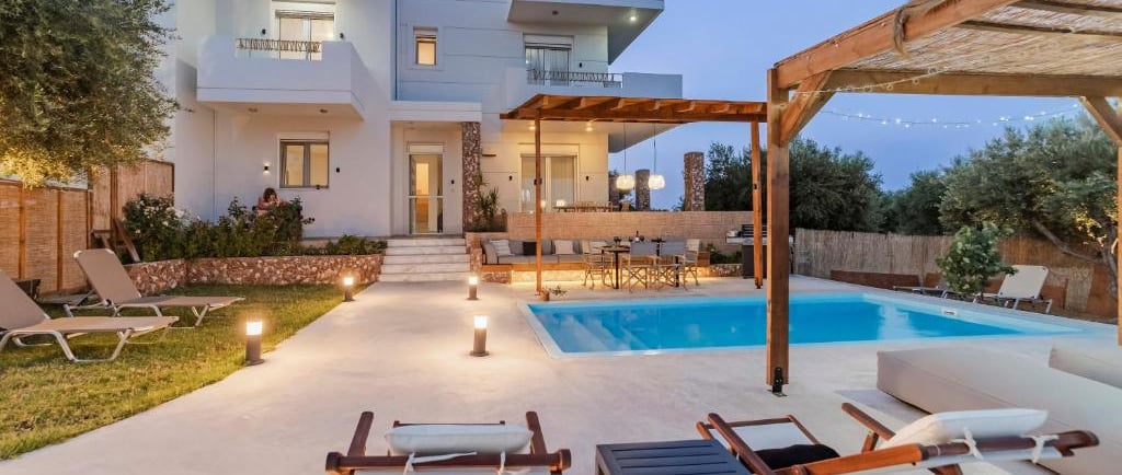Luxury modern villa with a private swimming pool, outdoor lounge, and patio at twilight.